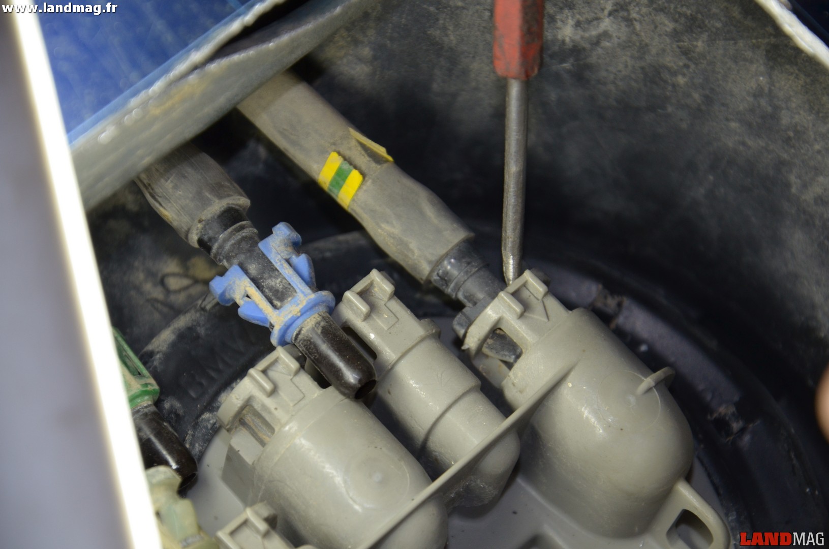 15- Avec une pointe, désengager délicatement les 2 pattes en plastique qui maintiennent les tuyaux de carburant en poussant sur leur base et retirer les tuyaux.